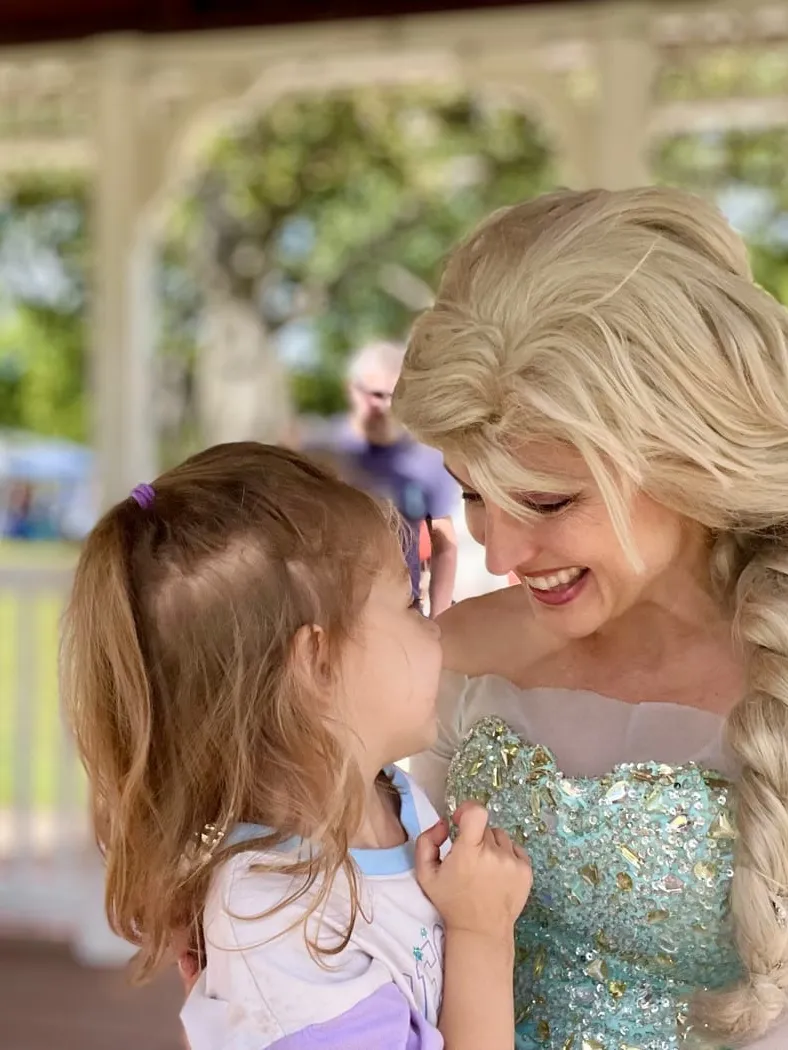 Elsa leaning down to talk with a small girl inside a park gazebo