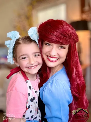 Ariel hugging a young girl with pink bows close together indoors