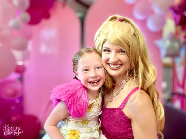 Barbie cheek to cheek with a grinning girl wearing a pink feather boa