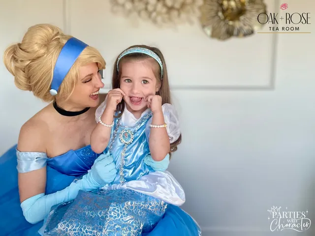 Cinderella laughing with a young girl mid-giggle in front of a floral wreath