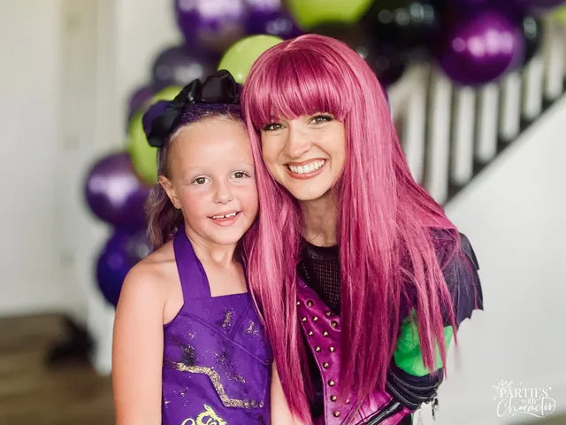 Mal smiling with a young girl in a sparkly purple and gold outfit