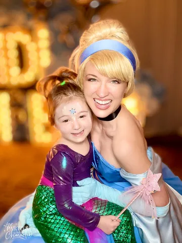 Cinderella smiling with a young girl dressed as a purple mermaid holding a wand