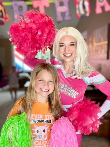 Addison and a young girl holding matching pom-poms at a party