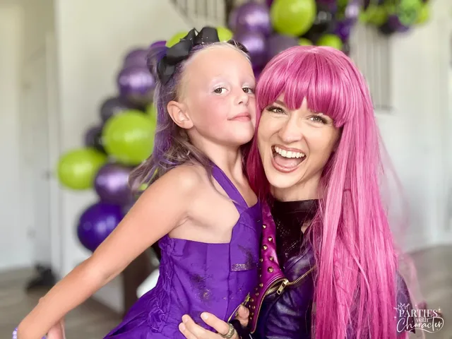 Mal laughing mid-motion while hugging a young girl in a purple party dress