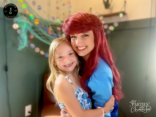 Ariel hugging an older girl in front of a teal party backdrop