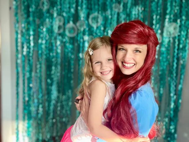 Ariel with a girl in a white dress against a shimmering teal curtain