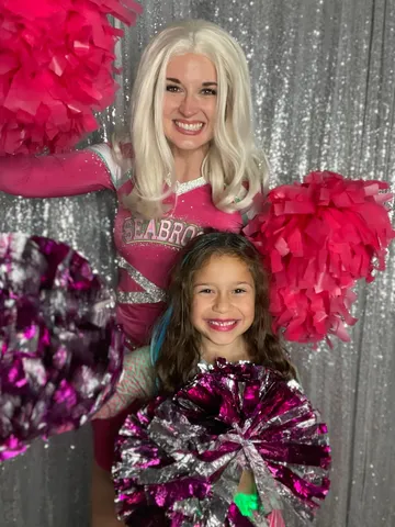 Addison and a girl shaking pink and silver pom-poms in front of a sequin backdrop