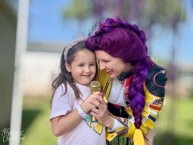 Rumi cheek to cheek with a girl in a pink shirt clutching a gold microphone