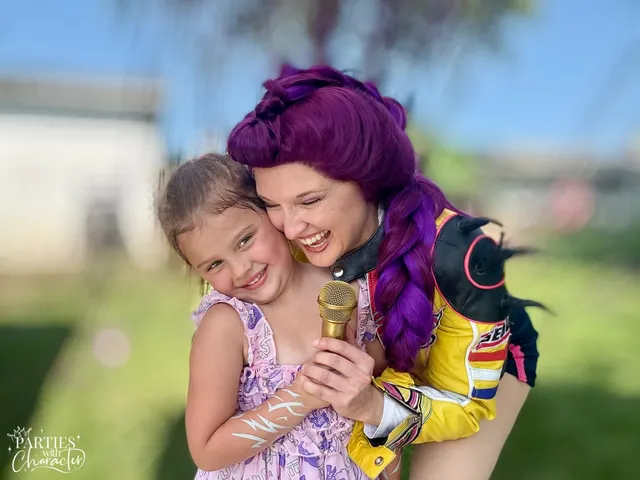 Rumi hugging a girl in a lavender dress while she sings into a gold microphone