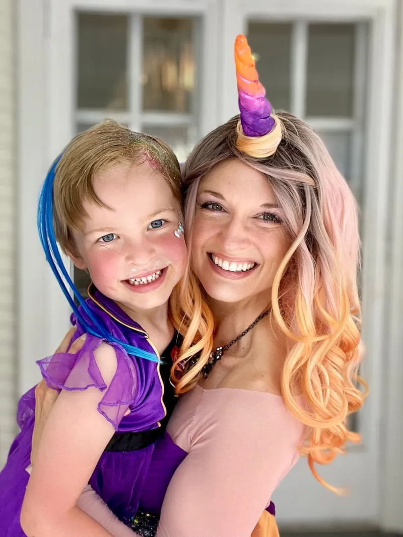 Unicorn Princess holding a grinning young girl in a purple dress with blue hair extensions on a porch