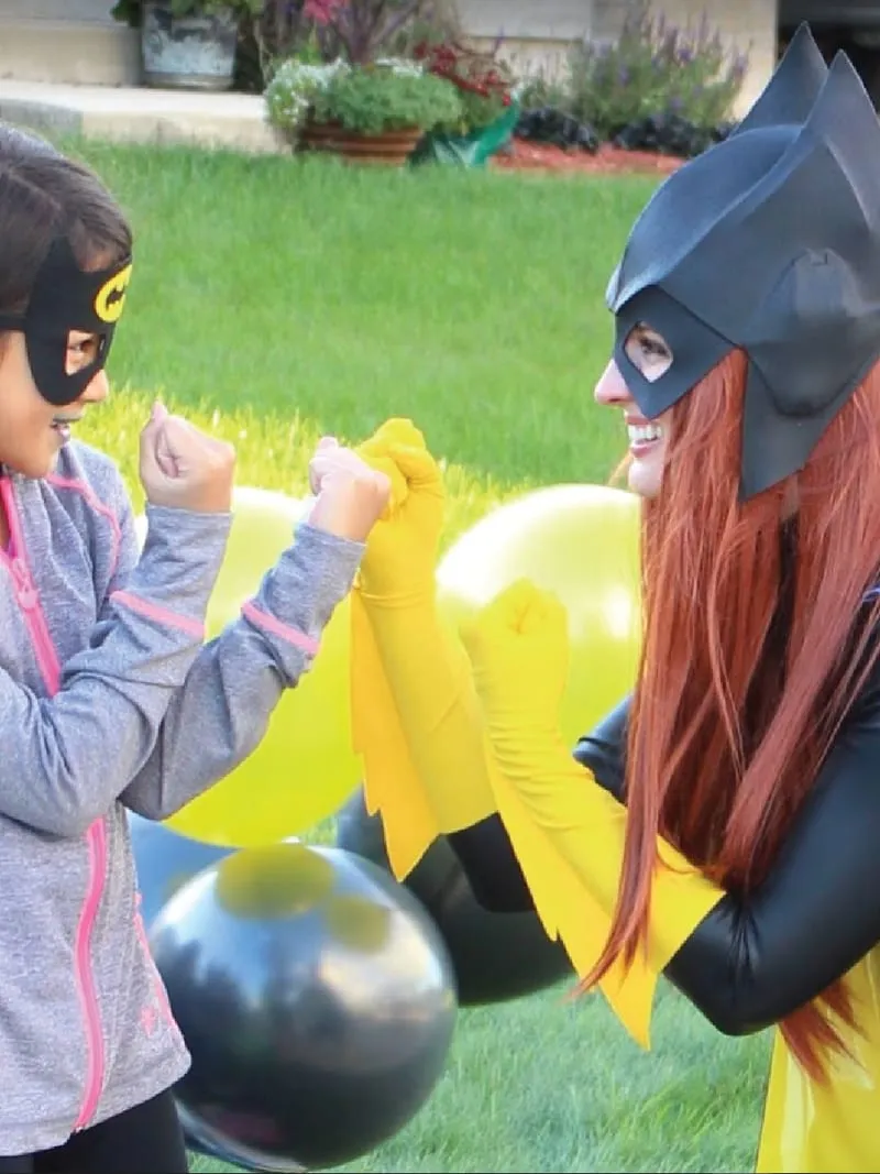 Batgirl fist-bumping a young girl wearing a Batgirl mask in a front yard