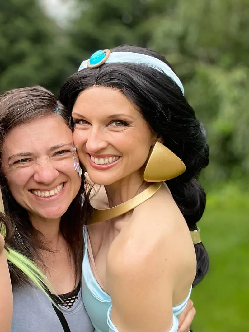 Jasmine from Aladdin cheek to cheek with a laughing mother on a sunny lawn
