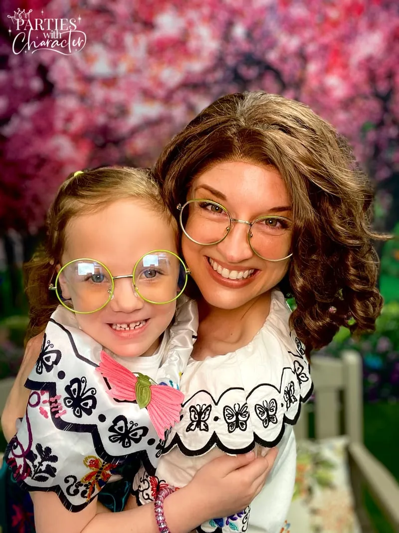 Mirabel hugging a young girl in front of a cherry blossom backdrop