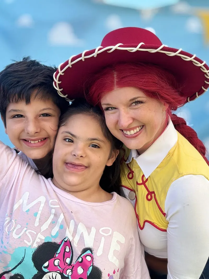 Jessie from Toy Story smiling with a young boy and a girl in a Minnie Mouse tee in front of a cloud-print backdrop
