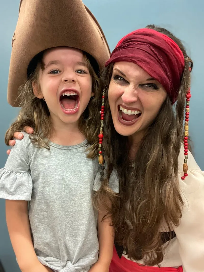 Pirate laughing open-mouthed beside a young girl wearing her oversized pirate hat